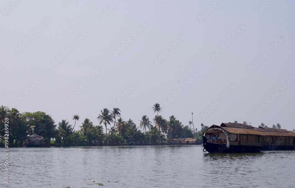 Panorama of the scenic backwaters in rural Kerala (India) with tropical palm trees, a luxurious house boat & a waterway leading to Kochi & Alleppey on a sunny summer day with a clear blue sky