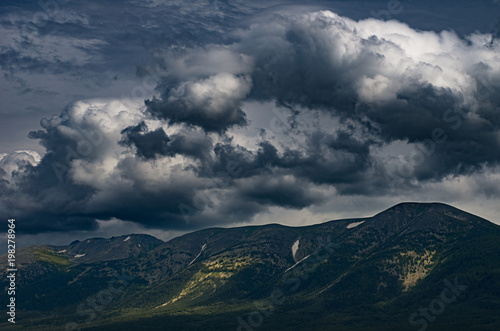 Scenic stormy cloudscape over mountains peaks with sunny highlights on the slopes