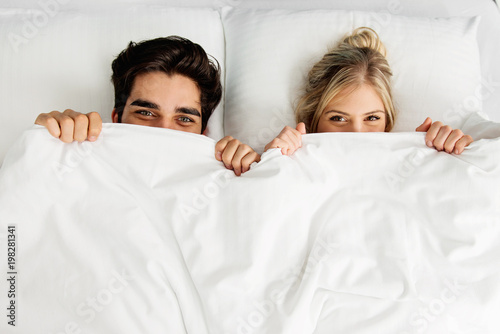 Young loving couple lying on the bed, peaking 