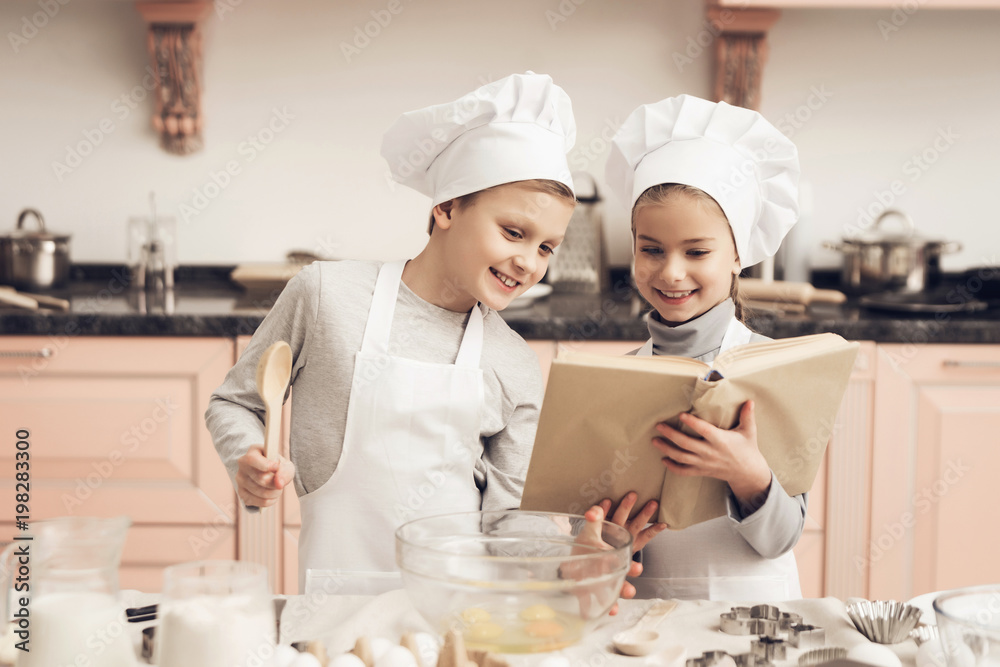 Children in kitchen. Brother and sister are reading cookbook while cooking. Children in kitchen. Brother and sister are reading cookbook while cooking.