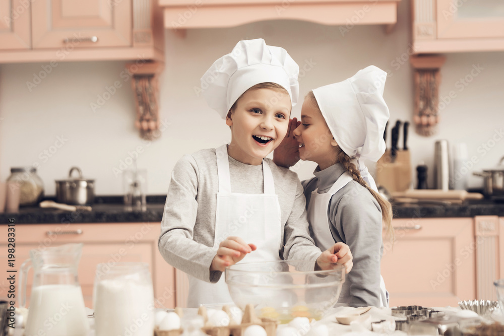 Children in kitchen. Sister is telling brother a secret while cooking. Children in kitchen. Sister is telling brother a secret while cooking.