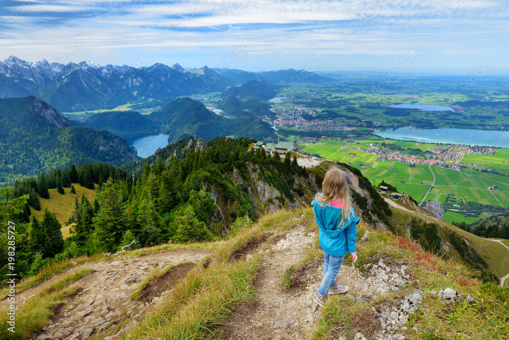 Cute little hiker enjoying picturesque views from the Tegelberg mountain, a part of Ammergau Alps, located nead Fussen town, Germany.
