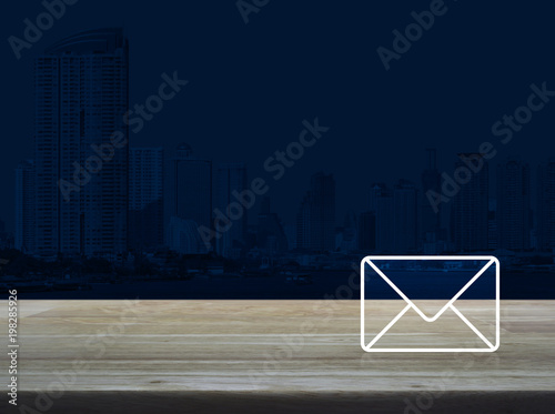 Mail icon on wooden table over modern office city tower background, Contact us concept