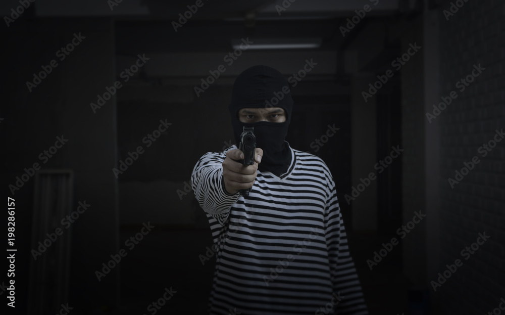 Mask thief with holding gun pointing to the target in front at dark construction site, Criminal robbery concept
