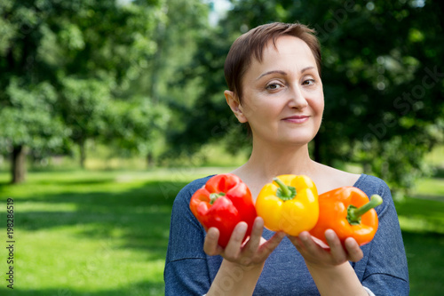 Middle aged woman holding vegetables / bell peppers/paprika. Portrait of happy 40 50 years old female in the summer/autumn garden. Healthy eating. Vegetarian food . Paleo diet. Raw food diet.