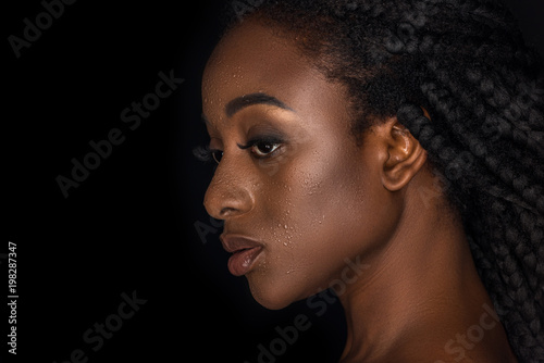 profile portrait of beautiful african american woman with water drops on face looking away isolated on black