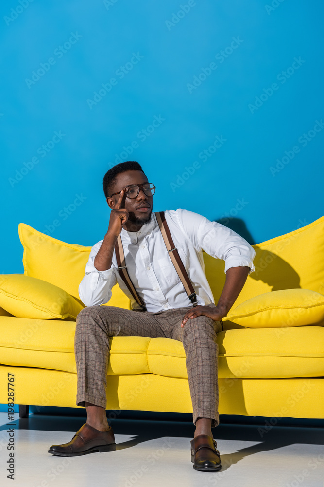 handsome stylish young african american man sitting on yellow couch on blue handsome stylish young african american man sitting on yellow couch on blue
