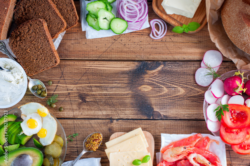 Ingredients for the preparation of a traditional Danish open sandwich called Smorrebrod on rye bread with vegetables, red fish, shrimps, eggs, herring and greens. Top view, horizontal, copy space. photo