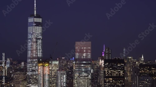 New York City low flying telephoto aerial view of Lower Manhattan Financial District office buildings with the Midtown Skyline in the background at night.