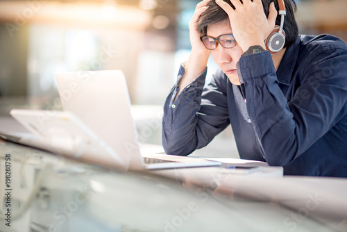 Young Asian business man feeling stressed and frustrated while working with laptop computer. Male entrepreneur getting in trouble with his job. freelance lifestyle in urban workspace.