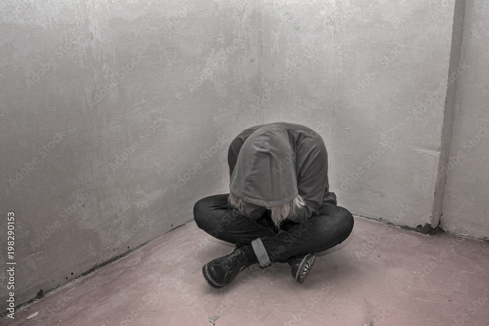 Photo of desperate young drug addict wearing hood and sitting alone in corner Photo of desperate young drug addict wearing hood and sitting alone in corner