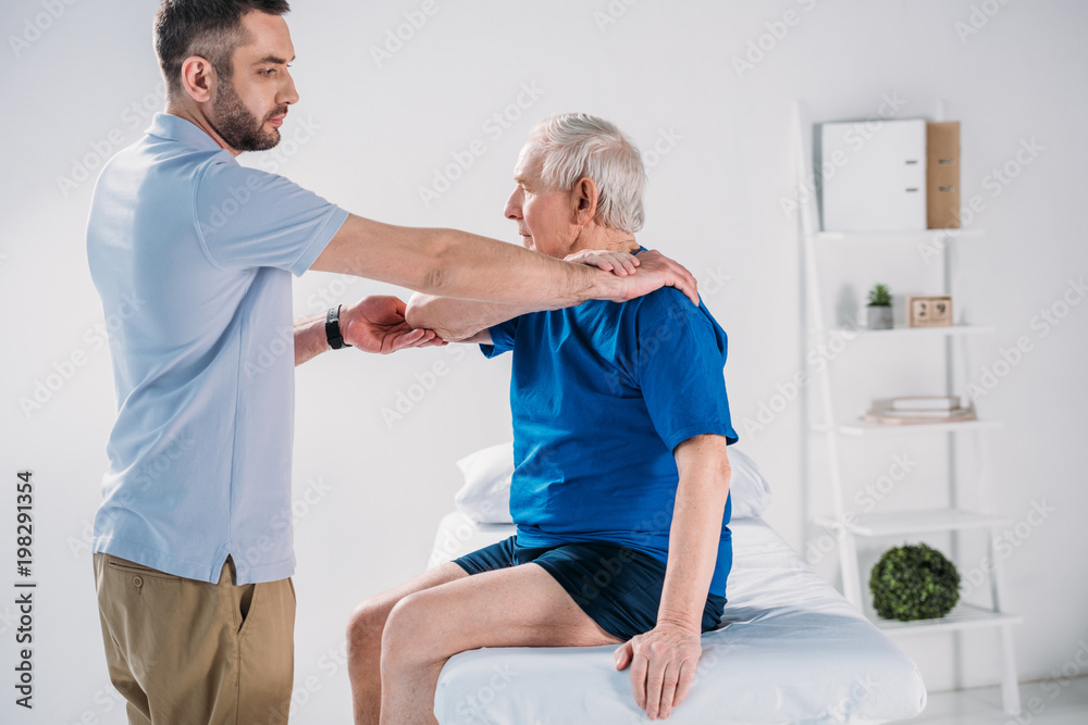 side view of rehabilitation therapist doing massage to senior man on massage table