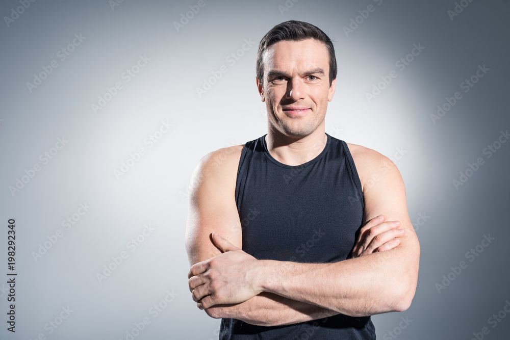 Fototapeta premium Sportsman standing with folded arms on grey background