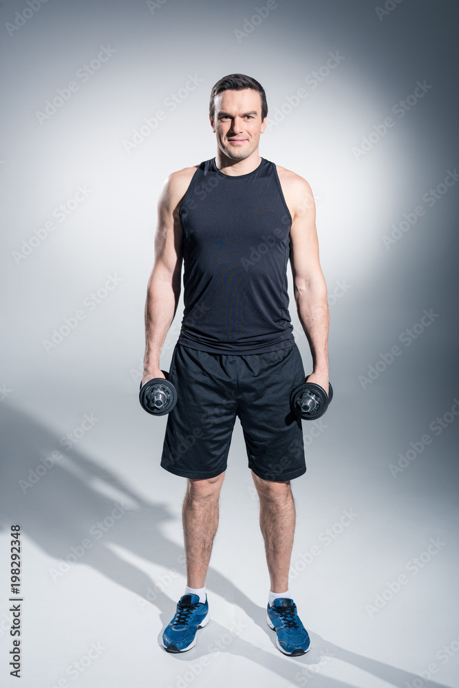Active man exercising with dumbbells on grey background