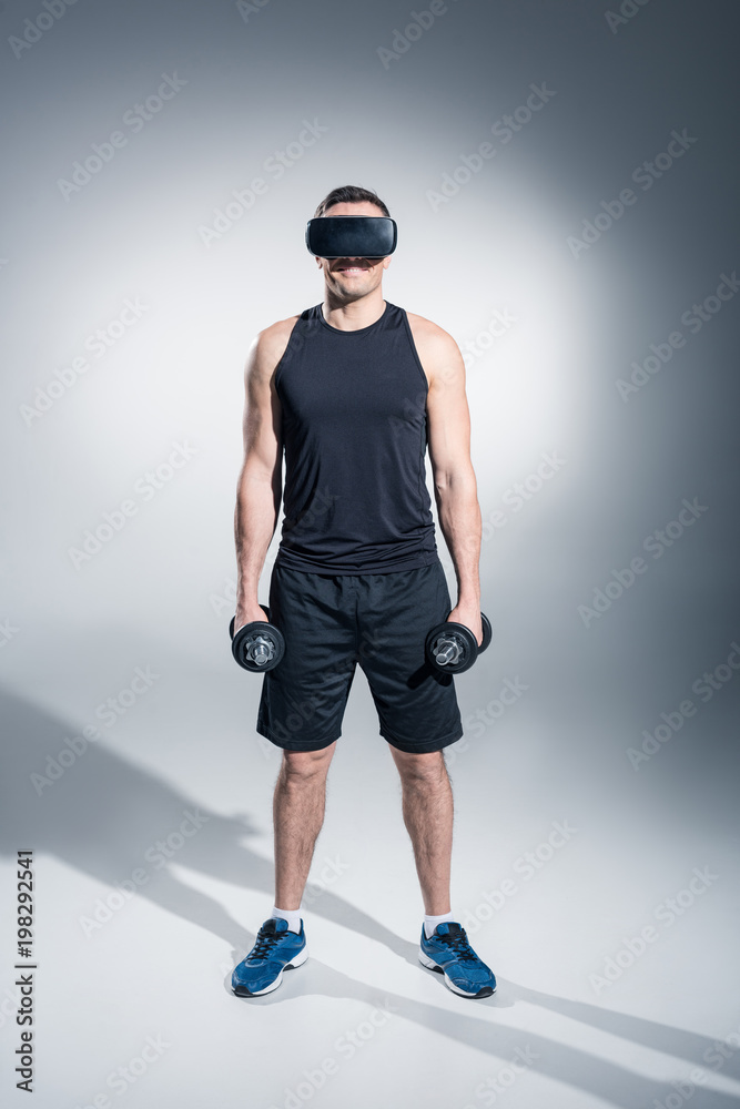 Sportive man exercising with dumbbells while wearing vr glasses on grey background Sportive man exercising with dumbbells while wearing vr glasses on grey background