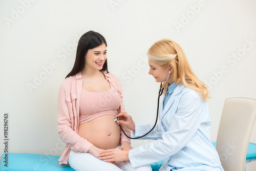 obstetrician gynecologist listening heartbeat of child fetus of pregnant woman with stethoscope