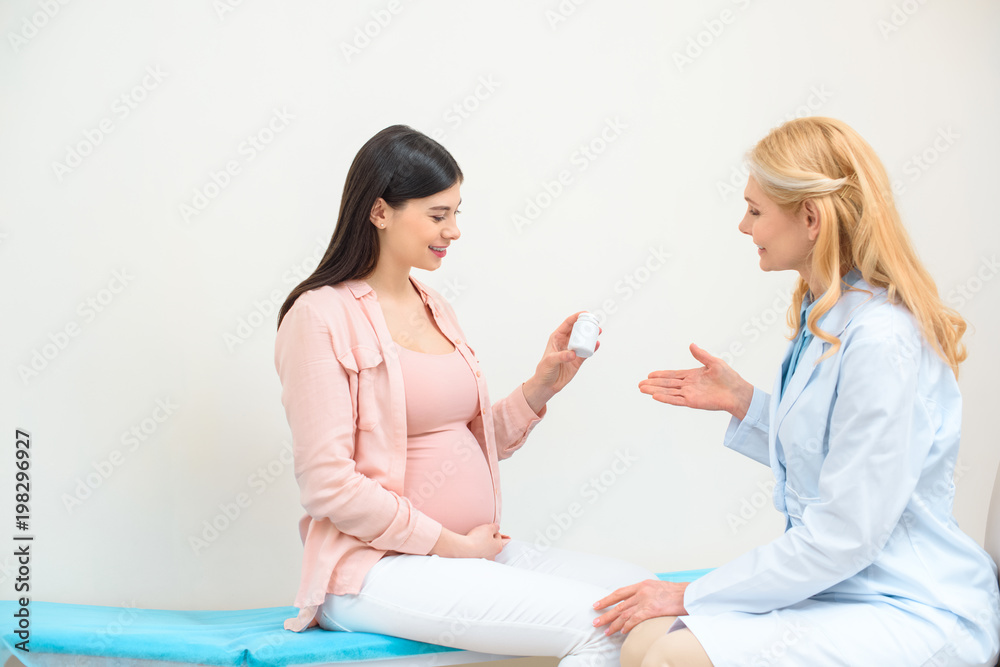obstetrician gynecologist showing jar of pills to pregnant woman obstetrician gynecologist showing jar of pills to pregnant woman