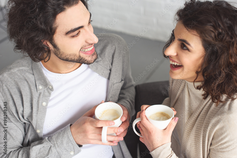 high angle view of young laughing couple drinking coffee at home high angle view of young laughing couple drinking coffee at home