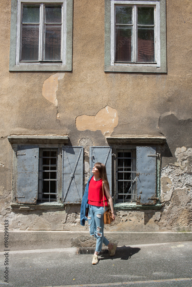 Young tourist girl walks by street A small town in the mountains of Slovenia, Europe. Shabby old houses facades, and roofs.