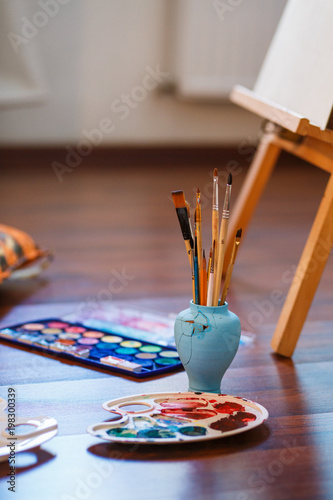 Paint Brushes on a table. Vertical photo. Easel, Canvas, paint, brushes, palette staying on the floor