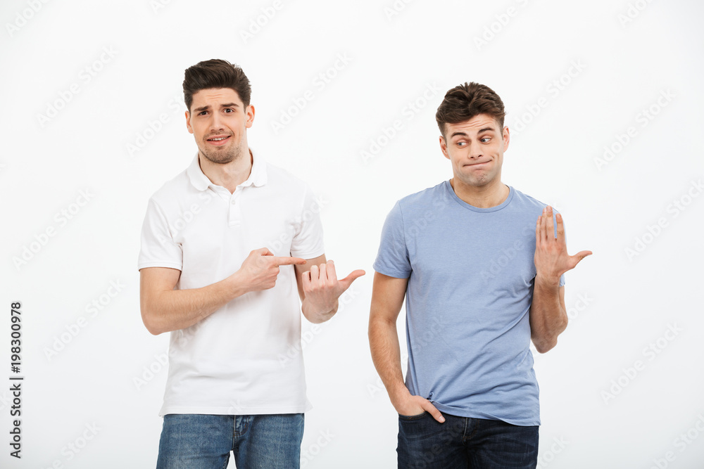 Portrait of two confused young men pointing fingers