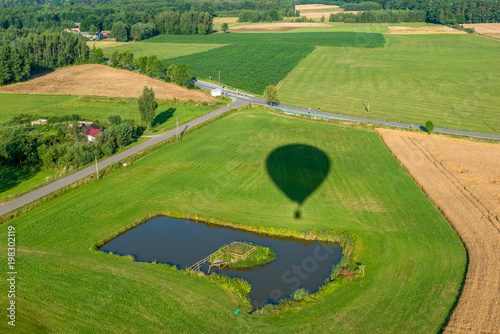 Cień balonu lecącego nad polami ze stawem, w dole widać drogi i pola uprawne.