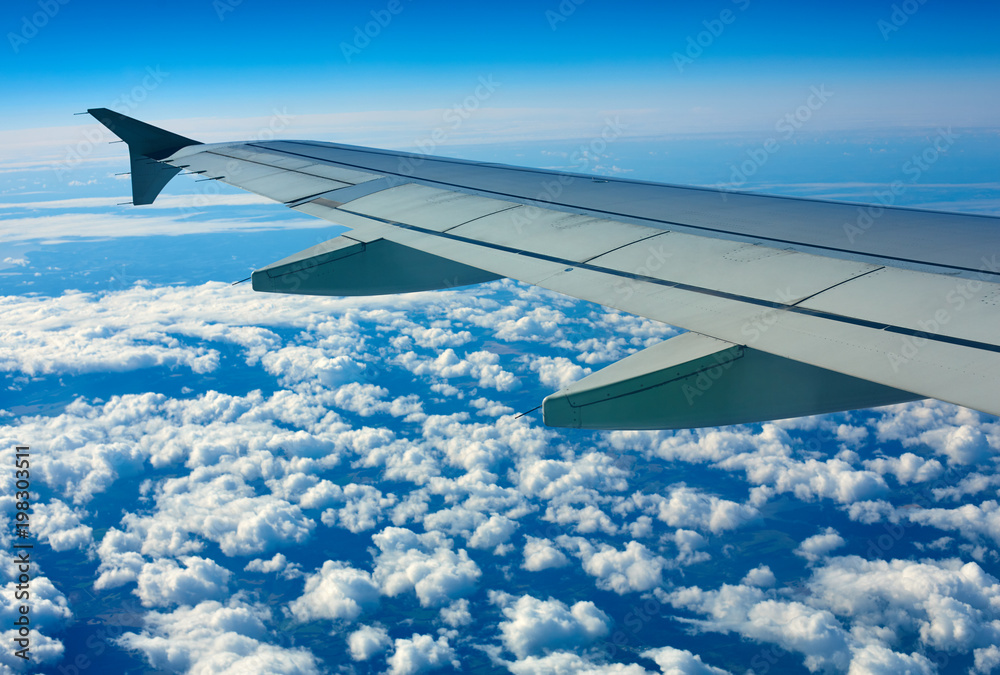 Obraz premium Airplane wing out of window, blue sky and clouds