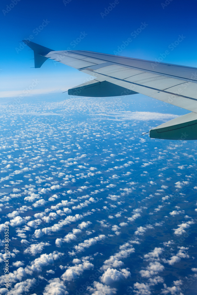 Airplane wing out of window, blue sky and clouds