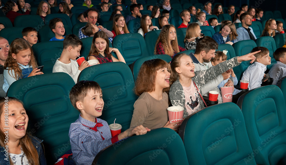 Close sideview of funny children watching fancy movie,sitting on the comfortable cinema places. Kids eating popcorn and drinking fizzy drinks. Look happy and satisfied. Close sideview of funny children watching fancy movie,sitting on the comfortable cinema places. Kids eating popcorn and drinking fizzy drinks. Look happy and satisfied.