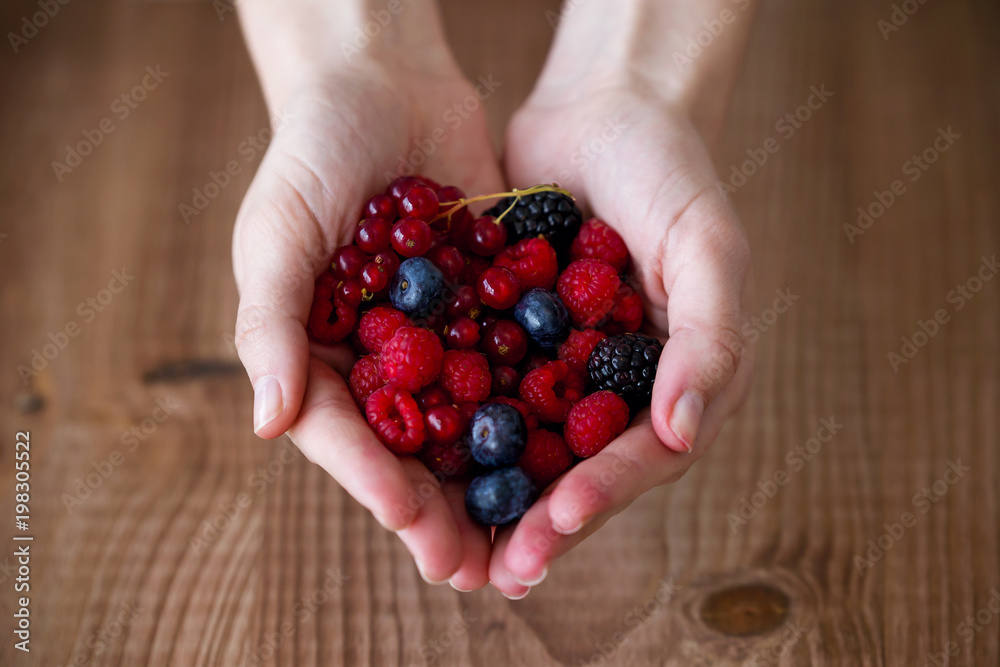 Some hands holding blueberries and raspberries over wooden background. Some hands holding blueberries and raspberries over wooden background.