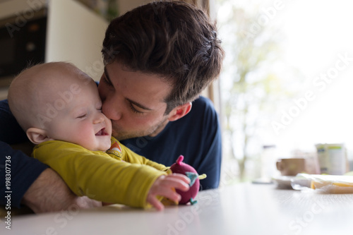 Young father kissing with baby boy at breakfast table