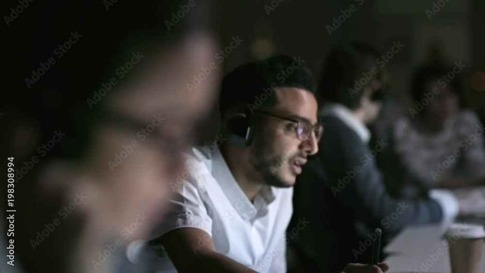 Tilt down with rack focus of male and female telemarketing agents in glasses making calls and talking on headsets Tilt down with rack focus of male and female telemarketing agents in glasses making calls and talking on headsets