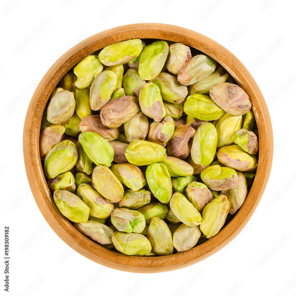 Shelled, roasted pistachios in wooden bowl. Green seeds and ripe fruits of Pistacia vera, used as snack. Isolated macro food photo close up from above on white background. Shelled, roasted pistachios in wooden bowl. Green seeds and ripe fruits of Pistacia vera, used as snack. Isolated macro food photo close up from above on white background.