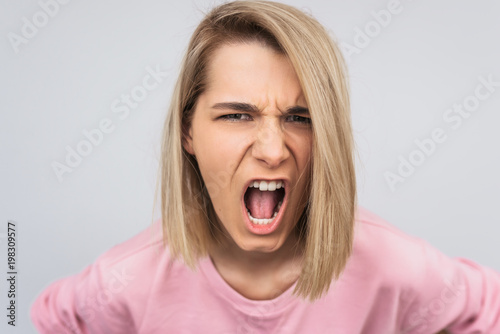 Closeup horizontal portrait of young blonde female screaming loud with angry face at the camera. Unhappy woman isolated on white studio background. Negative emotions, people and lifestyle concept.