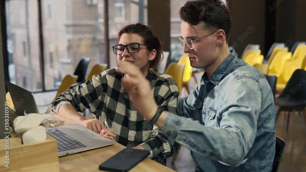 A couple of two young people wearing glasses, sitting next to each other, talking with someone through video chat. Enjoying time spent together. A couple of two young people wearing glasses, sitting next to each other, talking with someone through video chat. Enjoying time spent together.