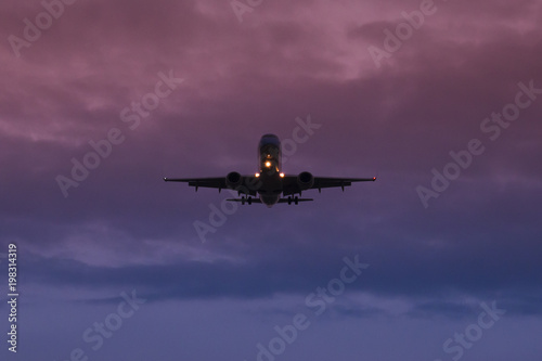A passenger plane takes off against the background of dusk and the dark blue and purple sky, view from below