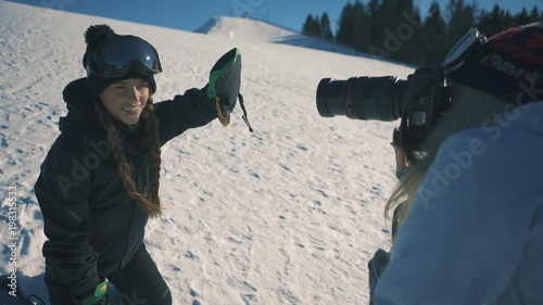 Attractive sporty female snowboarder or skier and photographer make photo session on ski resort on snowy mountains. Sunny day. mid shot