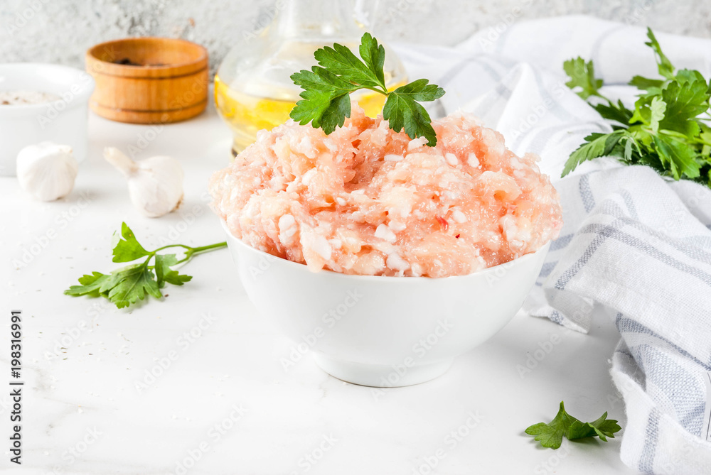 Raw chicken or turkey minced meat in white bowl, with oil, spices and herbs on light background. Copy space. Raw chicken or turkey minced meat in white bowl, with oil, spices and herbs on light background. Copy space.