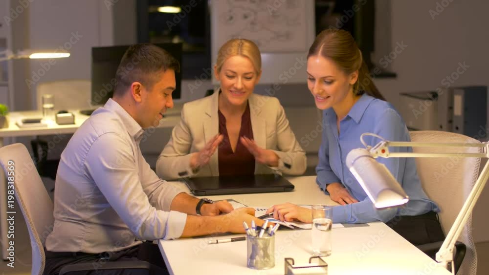 business, deadline and people concept - happy team with papers and laptop computer working late at night office business, deadline and people concept - happy team with papers and laptop computer working late at night office