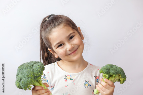 Happy little girl eating fresh vegetables. A portrait of cute child girl on a white background. Healthy teeth.
