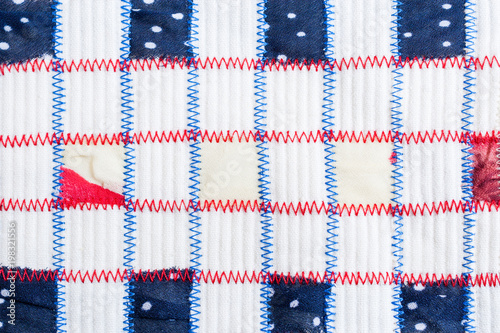Square pieces of colored fabrics, sewn by red and blue zigzag seams on relief white fabric. © SeNata