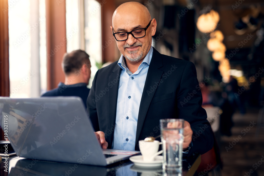 Mature professional businessman is using a laptop and drinking coffee in the coffee shop. Mature professional businessman is using a laptop and drinking coffee in the coffee shop.