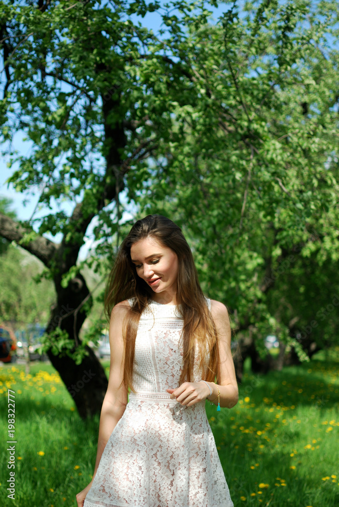 Beautiful smiling brunette girl standing in the alley in the summer background. Beautiful smiling brunette girl standing in the alley in the summer background.