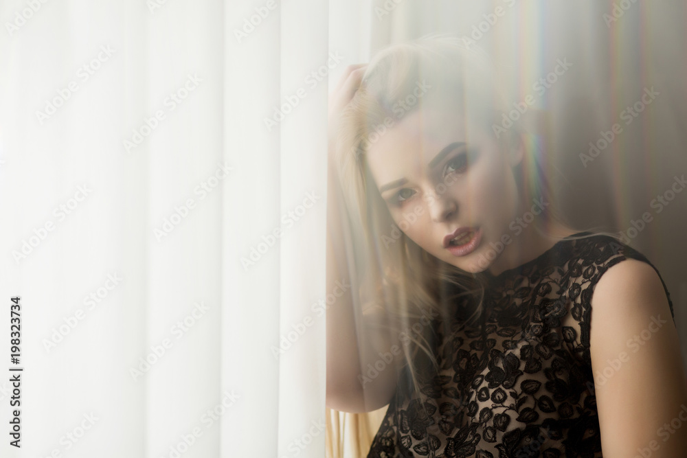 Glorious young lady in lace blouse posing near the window with curtain. Space for text Glorious young lady in lace blouse posing near the window with curtain. Space for text