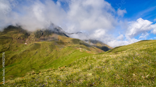 mountain landscape and fresh alpine spring grass with buttercups against the backdrop of mountain slopes and rain clouds