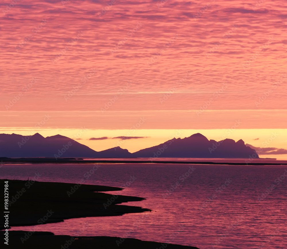 Incredibly beautiful dawn (sunset) on the shore of the Atlantic Ocean. Silhouettes of mountains and red clouds. Iceland.
