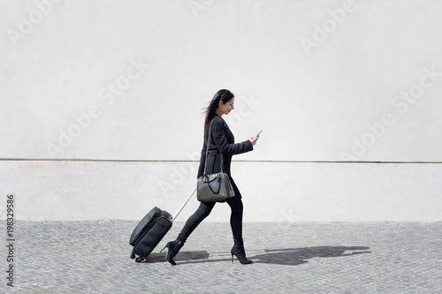 Executive and modern woman walks the street with her luggage while texting the mobile phone.
