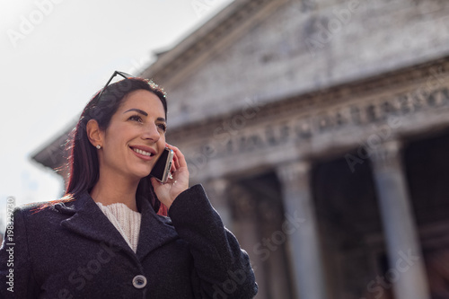 Young charming executive women talks by a mobile phone (cell phone) and smile while visit the Pantheon in Rome, Italy