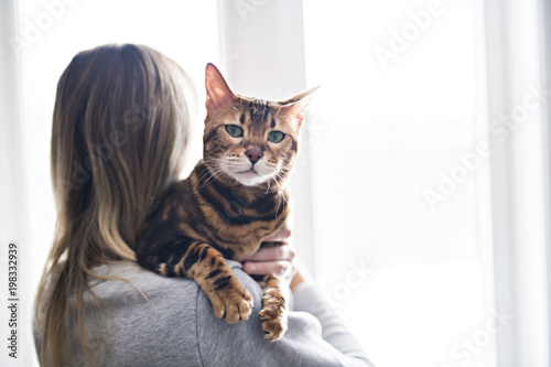 Young woman holding cat close to a window at home
