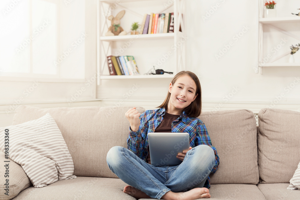 Little girl using digital tablet on sofa at home